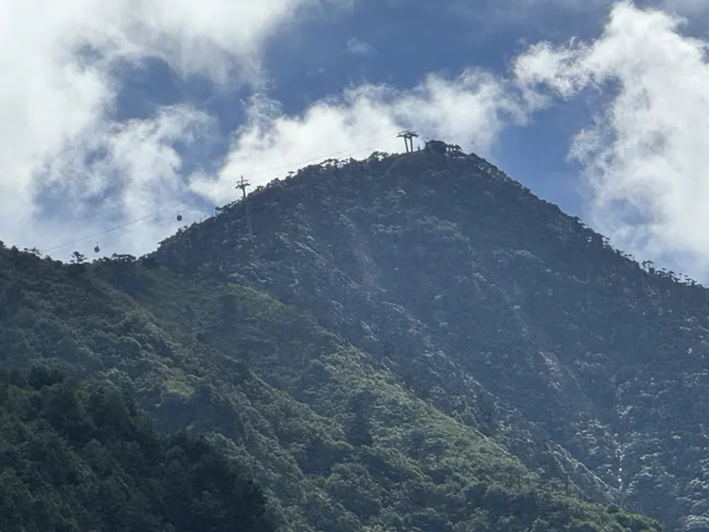 Sunlight and clouds above a forested peak.